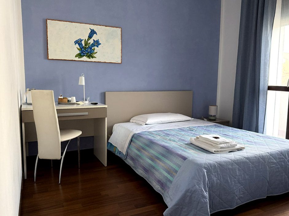 Camera Genziana, letto con copriletto azzurro, scrivania e quadro di genziane